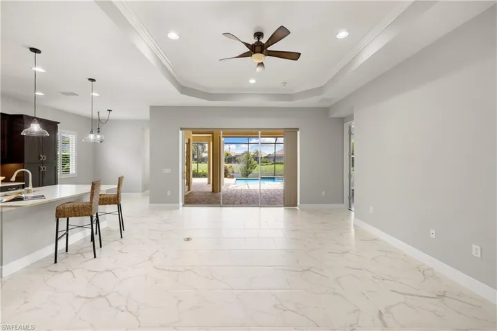 Living room with a tray ceiling, sink, crown molding, light tile patterned flooring, and ceiling fan