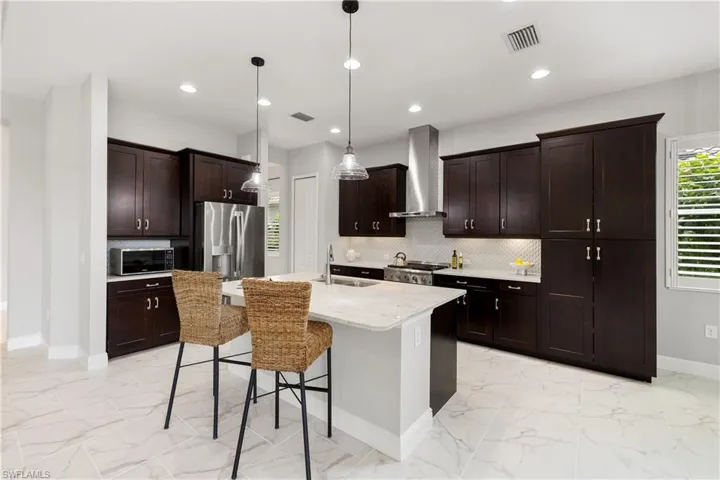 Kitchen featuring a breakfast bar, backsplash, a kitchen island with sink, appliances with stainless steel finishes, and wall chimney exhaust hood