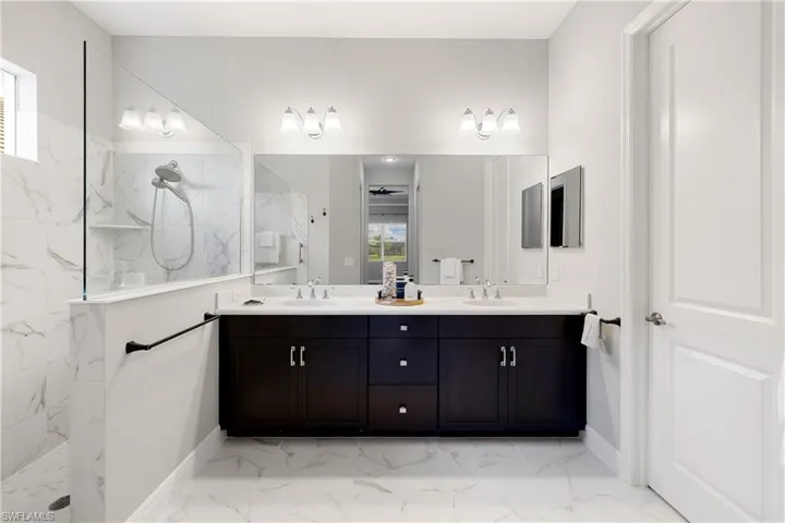 Owners bathroom featuring tile patterned flooring, tiled shower, and dual bowl vanity