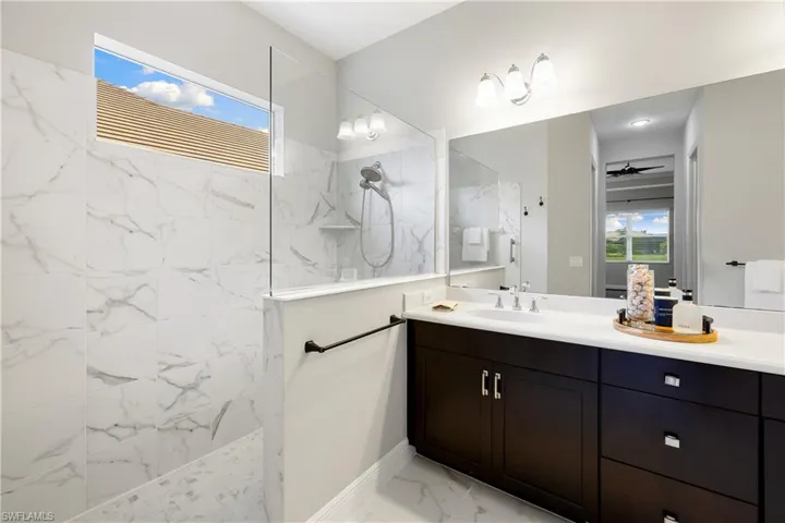 Owners bathroom featuring vanity, ceiling fan, tile patterned flooring, and a tile shower