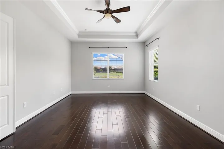 Owners suite with ornamental molding, ceiling fan, a raised ceiling, and hardwood / wood-style floors
