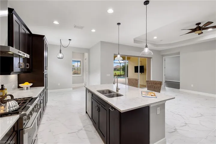 Kitchen with range with two ovens, wall chimney range hood, sink, a raised ceiling, and a center island with sink