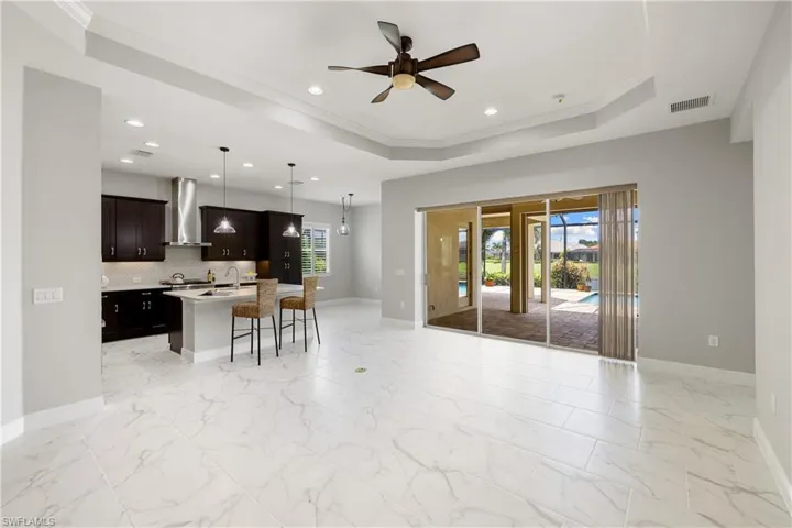 Kitchen with light tile patterned floors, a kitchen island with sink, a kitchen breakfast bar, a tray ceiling, and range hood