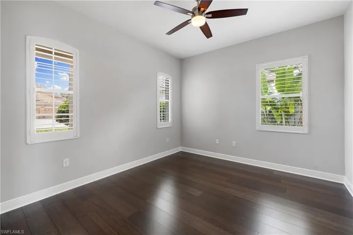 Den with dark wood-type flooring and ceiling fan