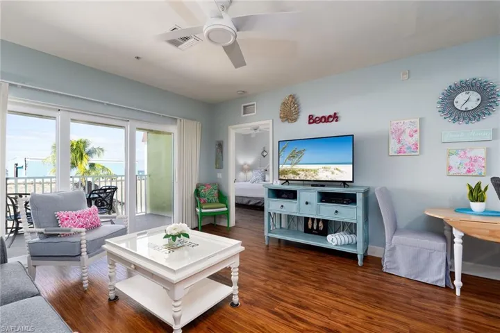 Living area featuring wood-finish flooring, a ceiling fan, and sliding glass doors opening to a balcony with water scenery