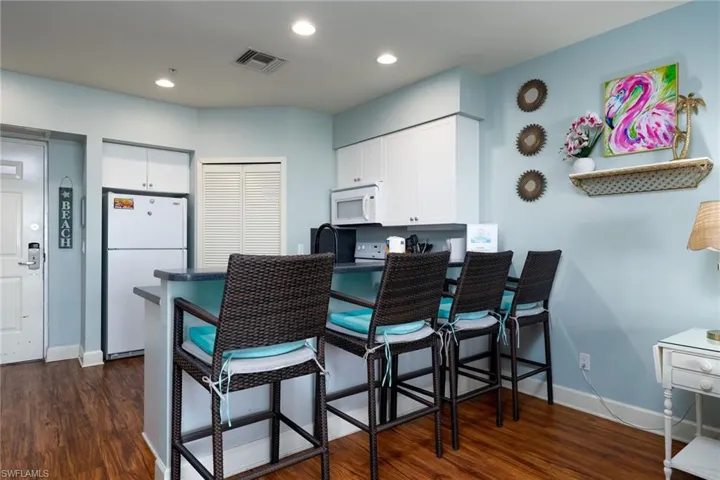 Kitchen features a breakfast bar with seating for four, white upper cabinetry, and recessed lighting