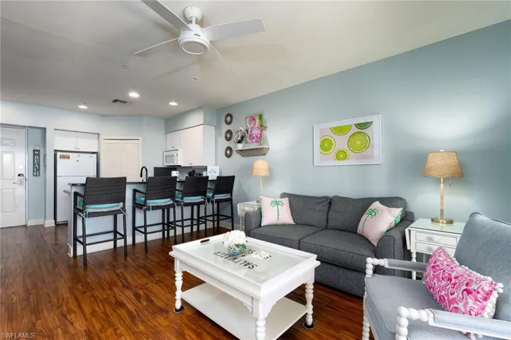 Open-concept living space featuring wood-finish flooring, a contemporary ceiling fan, recessed lighting, white upper and lower cabinetry, and a black countertop with a breakfast bar