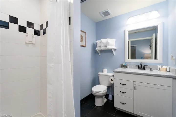 Bathroom featuring a white shower with a black and white checkerboard tile accent, a white vanity with a gray countertop, a white framed mirror, and dark tile flooring