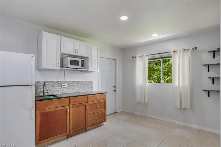 Kitchen featuring backsplash, sink, white appliances, and light tile floors