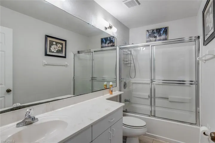Full bathroom with shower / bath combination with glass door, tile flooring, oversized vanity, and toilet