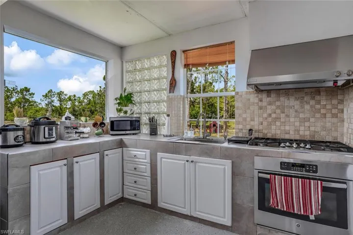 Kitchen with backsplash, wall chimney exhaust hood, white cabinets, sink, and appliances with stainless steel finishes