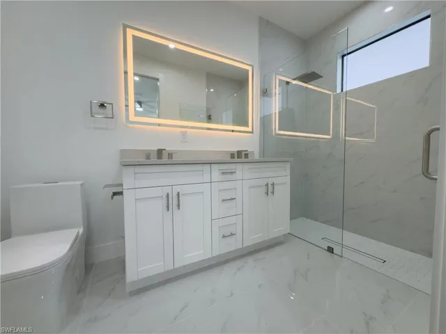 Bathroom with double vanity, light marble finish flooring, and a marble finish shower