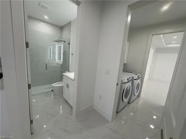 Bathroom with vanity, light marble finish floors, a marble finish shower, washing machine and dryer, and recessed lighting