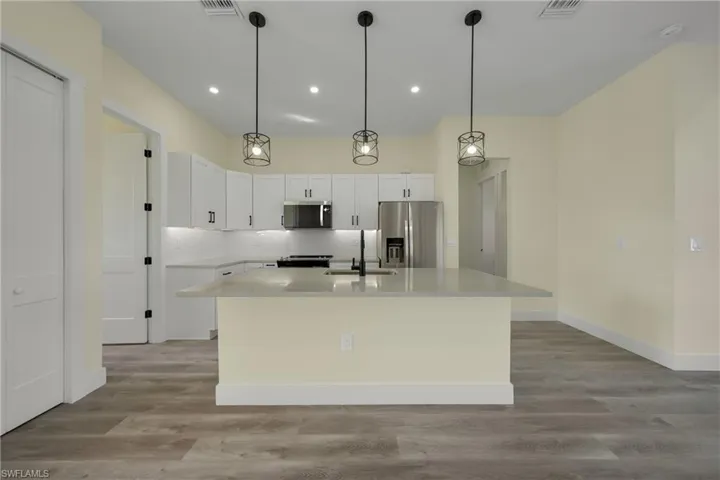 Kitchen featuring stainless steel appliances, tasteful backsplash, a kitchen island with sink, light stone counters, and decorative light fixtures