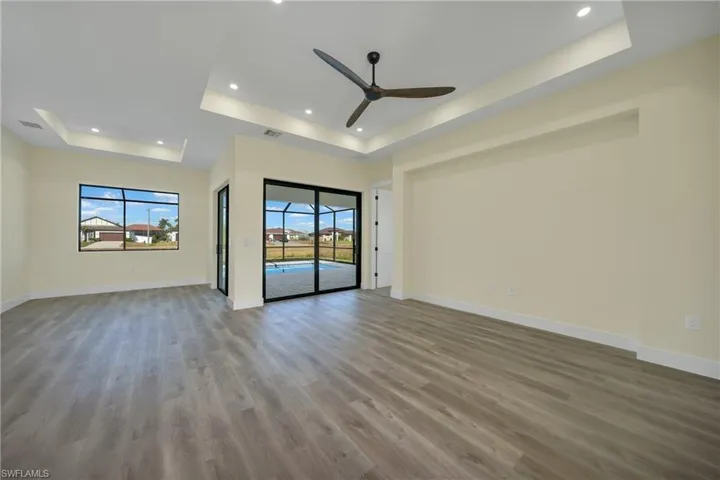 Empty room with a tray ceiling, light wood-style floors, a ceiling fan, and recessed lighting