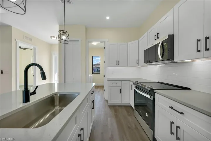 Kitchen featuring appliances with stainless steel finishes, white cabinetry, light stone counters, pendant lighting, and light wood-style floors