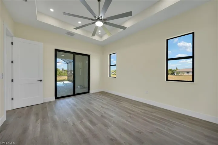 Empty room with a tray ceiling, light wood-style floors, recessed lighting, and a ceiling fan