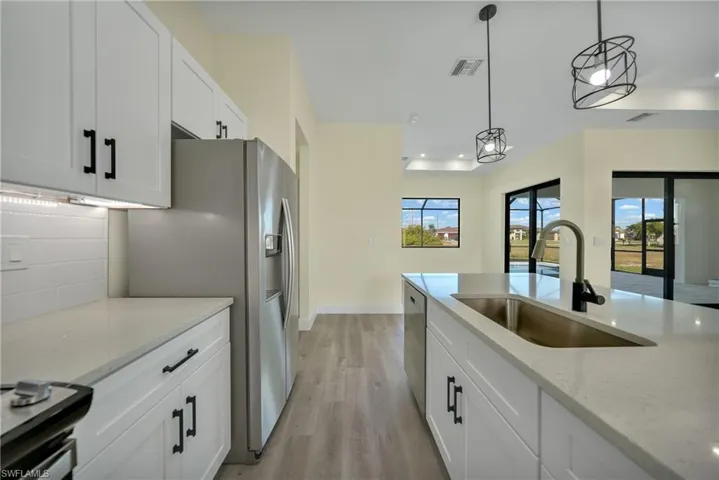 Kitchen with white cabinets, light stone counters, decorative light fixtures, light wood-style flooring, and recessed lighting