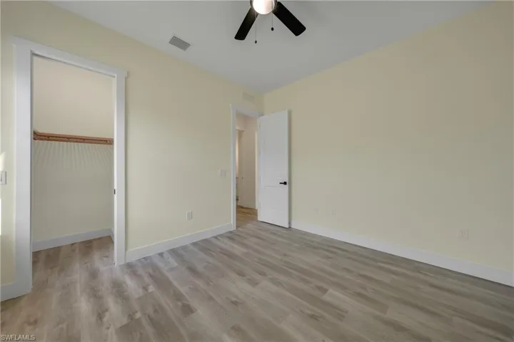 Unfurnished bedroom with light wood finished floors, a spacious closet, and a ceiling fan