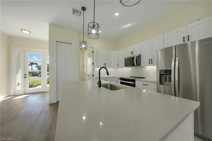 Kitchen with stainless steel appliances, decorative backsplash, white cabinetry, hanging light fixtures, and light stone countertops