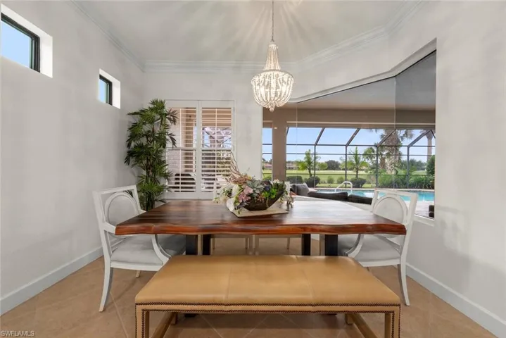 Tray ceiling with crown molding, chandelier, window with plantation shutters, tiled flooring, and screened outdoor area with pool