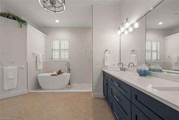 Freestanding soaking tub, dual vanity with quartz countertops and undermount sinks, plantation shutters, and tiled flooring