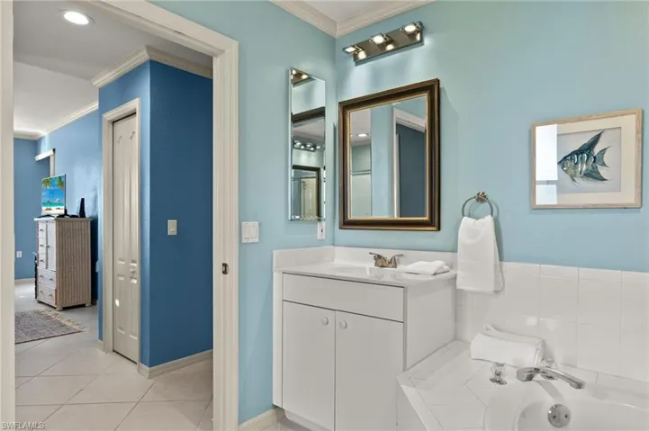 Bathroom featuring tile patterned floors, vanity, crown molding, and tiled tub