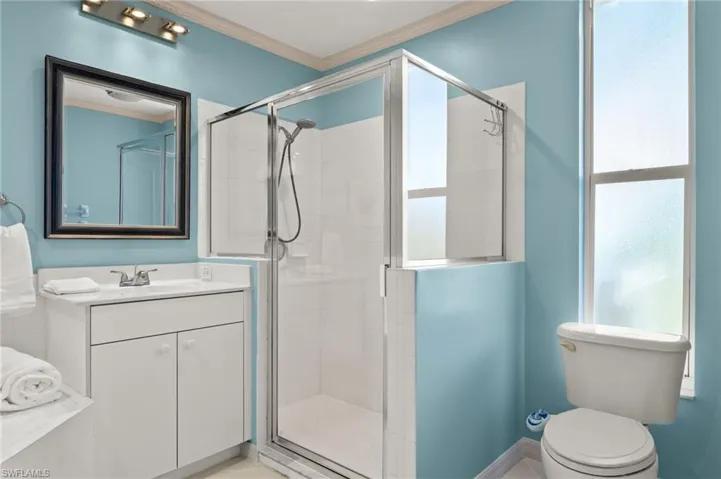 Bathroom with tile patterned flooring, crown molding, an enclosed shower, toilet, and vanity