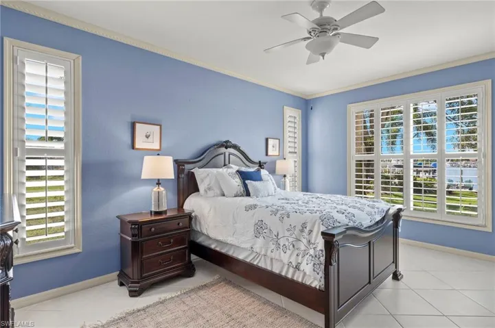 Tiled bedroom featuring ceiling fan, ornamental molding, and multiple windows