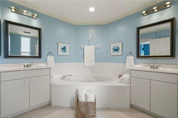 Bathroom with tile patterned flooring, vanity, crown molding, and tiled bath