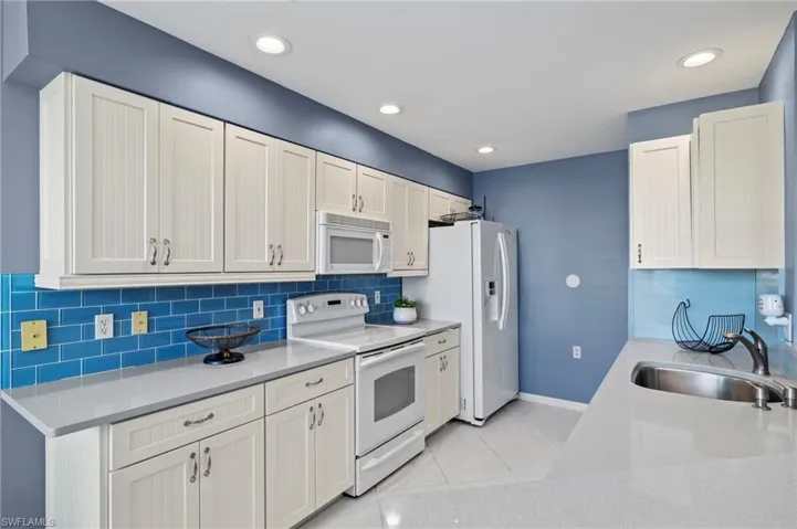 Kitchen with white cabinets, white appliances, sink, and light tile patterned floors