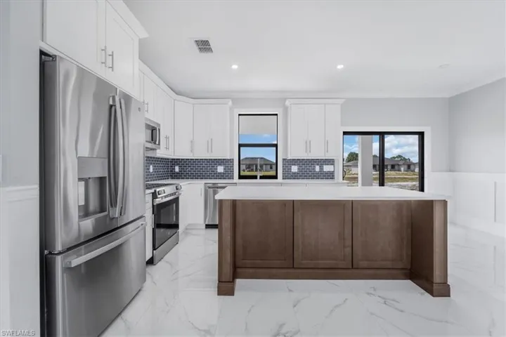 Dual tone kitchen with stainless steel appliances, light marble finish floors, a center island, wainscoting, and recessed lighting