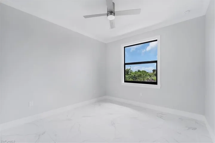 Empty room with crown molding, light marble finish flooring, and ceiling fan