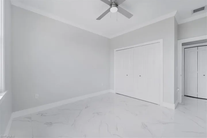 Unfurnished bedroom featuring crown molding, light marble finish flooring, a closet, and ceiling fan