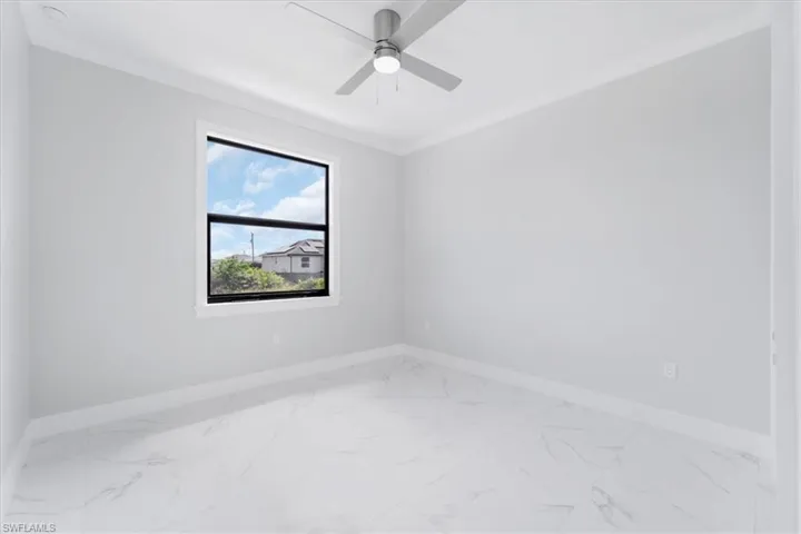 Spare room featuring light marble finish flooring, ornamental molding, and a ceiling fan