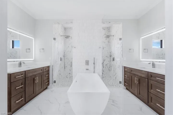 Full bath featuring healthy amount of natural light, a soaking tub, two vanities, a marble finish shower, and crown molding