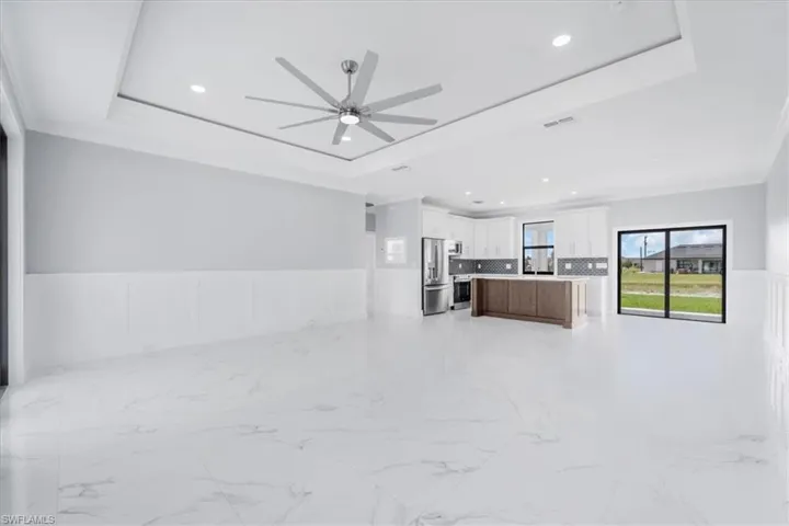 Kitchen featuring wainscoting, open floor plan, a decorative wall, ceiling fan, and light countertops