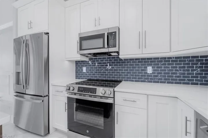 Kitchen featuring stainless steel appliances, white cabinetry, and light stone counters