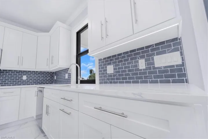 Kitchen with light stone countertops, white cabinets, light marble finish flooring, tasteful backsplash, and stainless steel dishwasher