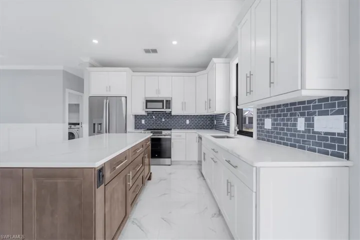 Two tone kitchen featuring dual tone cabinetry, stainless steel appliances, light stone counters, light marble finish flooring, and crown molding