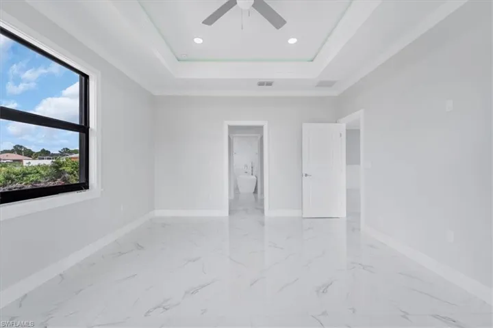 Unfurnished bedroom featuring a ceiling fan, crown molding, ensuite bathroom, recessed lighting, and a raised ceiling
