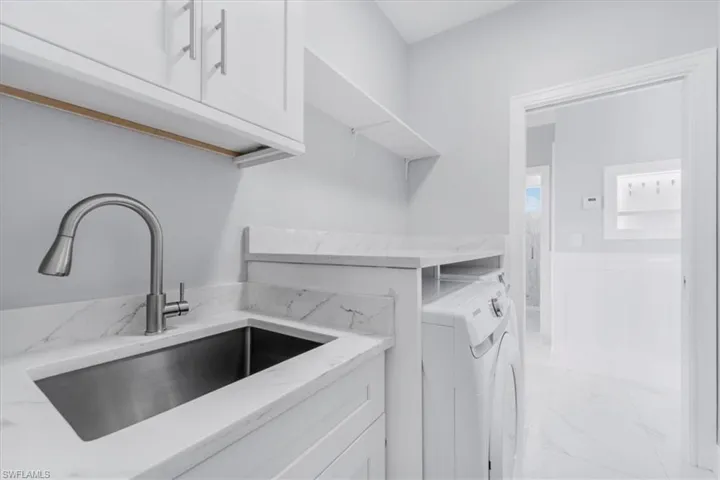 Laundry room with cabinet space, light marble finish flooring, and washing machine and clothes dryer