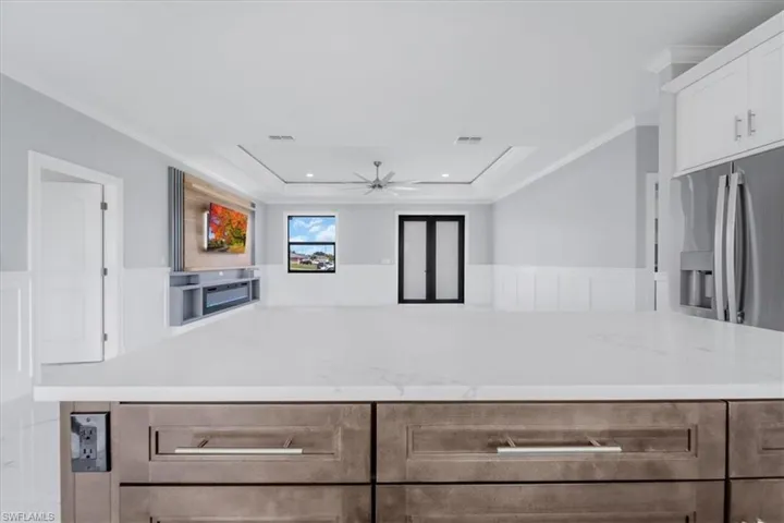 Kitchen featuring a ceiling fan, a kitchen island, stainless steel refrigerator with ice dispenser, wainscoting, and crown molding