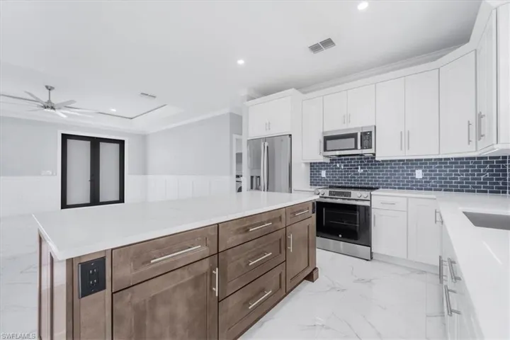 Dual tone kitchen with dual tone cabinets, stainless steel appliances, a wainscoted wall, crown molding, and a kitchen island