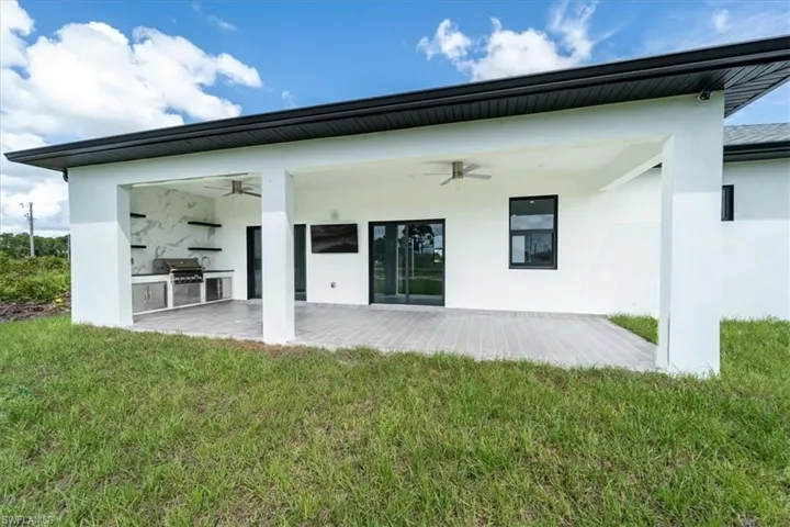 Back of house with a ceiling fan, exterior kitchen, stucco siding, a lawn, and a patio area