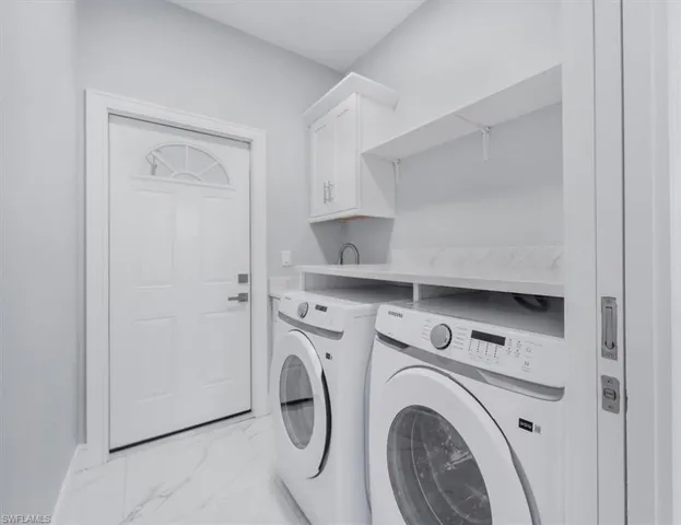 Laundry room with cabinet space, light marble finish flooring, and washing machine and clothes dryer