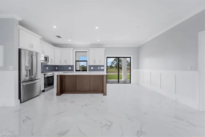 Kitchen featuring stainless steel appliances, ornamental molding, open floor plan, a center island, and wainscoting