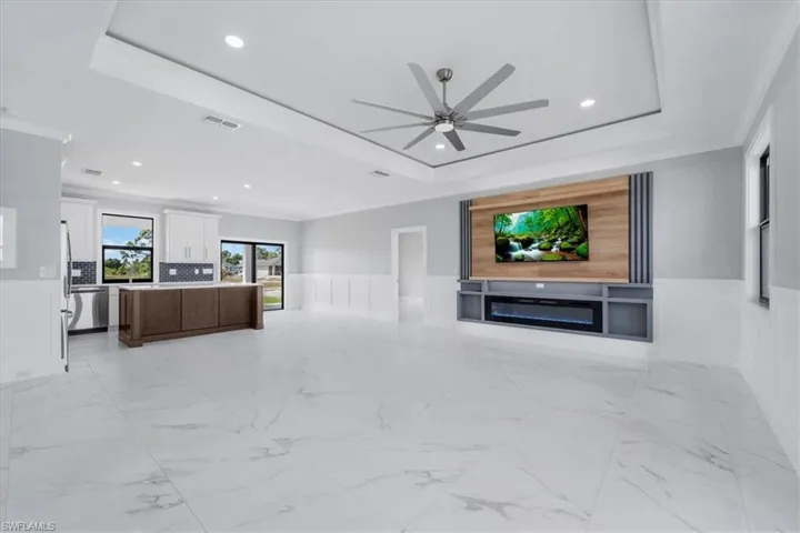 Unfurnished living room featuring wainscoting, a ceiling fan, recessed lighting, crown molding, and a raised ceiling