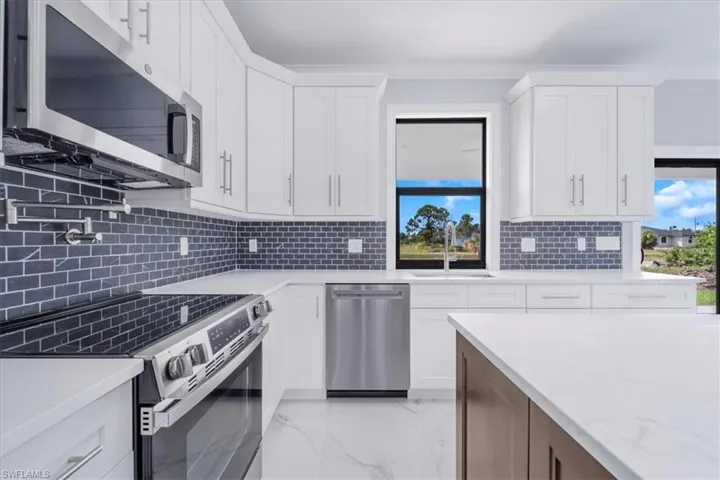 Kitchen featuring stainless steel appliances, light marble finish floors, dual tone cabinets, light stone counters, and decorative backsplash