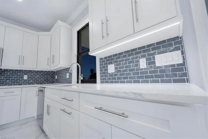 Kitchen with white cabinets, light stone counters, tasteful backsplash, crown molding, and light marble finish flooring